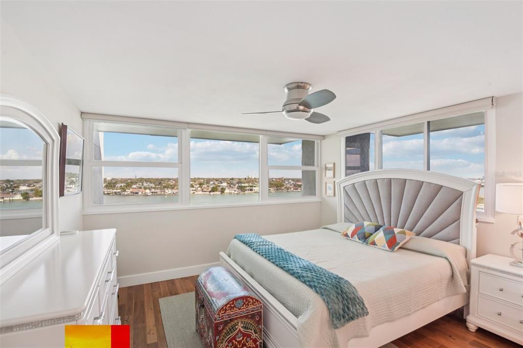 A bedroom with a bed, dresser, ceiling fan, and large windows overlooking a waterfront view — 500 TREASURE ISLAND CAUSEWAY UNIT 711, TREASURE ISLAND, FL