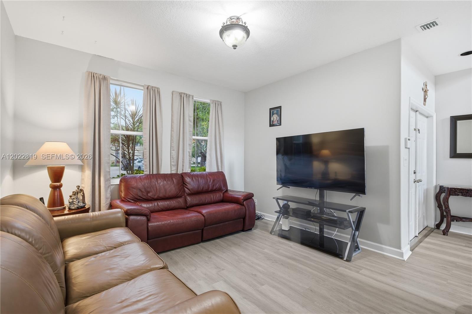 A living room features light wood-look flooring, two leather sofas, and a wall-mounted television — 16928 SW 35th St, Miramar FL 33027, MIRAMAR, FL