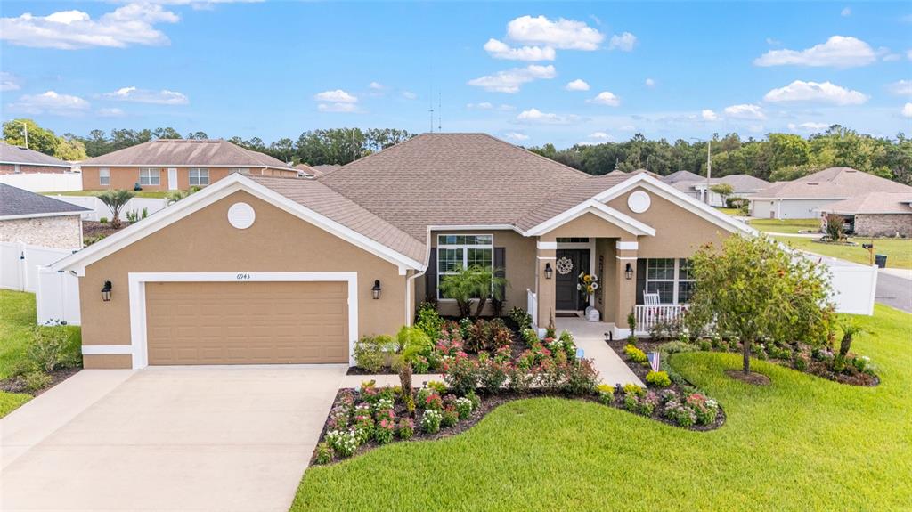 A tan single-story house with a two-car garage and landscaped front yard — 6943 SE 11TH PLACE, OCALA, FL