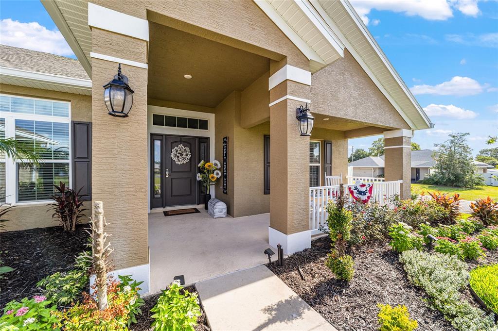 A covered front porch with a dark door, white railing, and landscaped garden beds — 6943 SE 11TH PLACE, OCALA, FL
