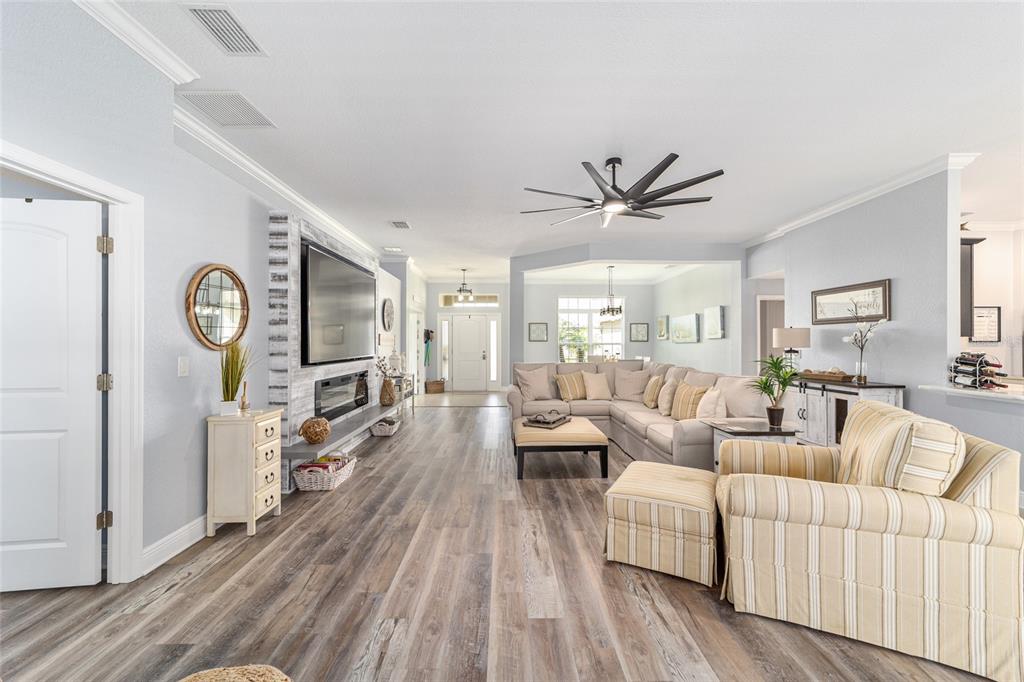 A spacious living room features light wood-look flooring, a fireplace wall, and neutral furniture — 6943 SE 11TH PLACE, OCALA, FL