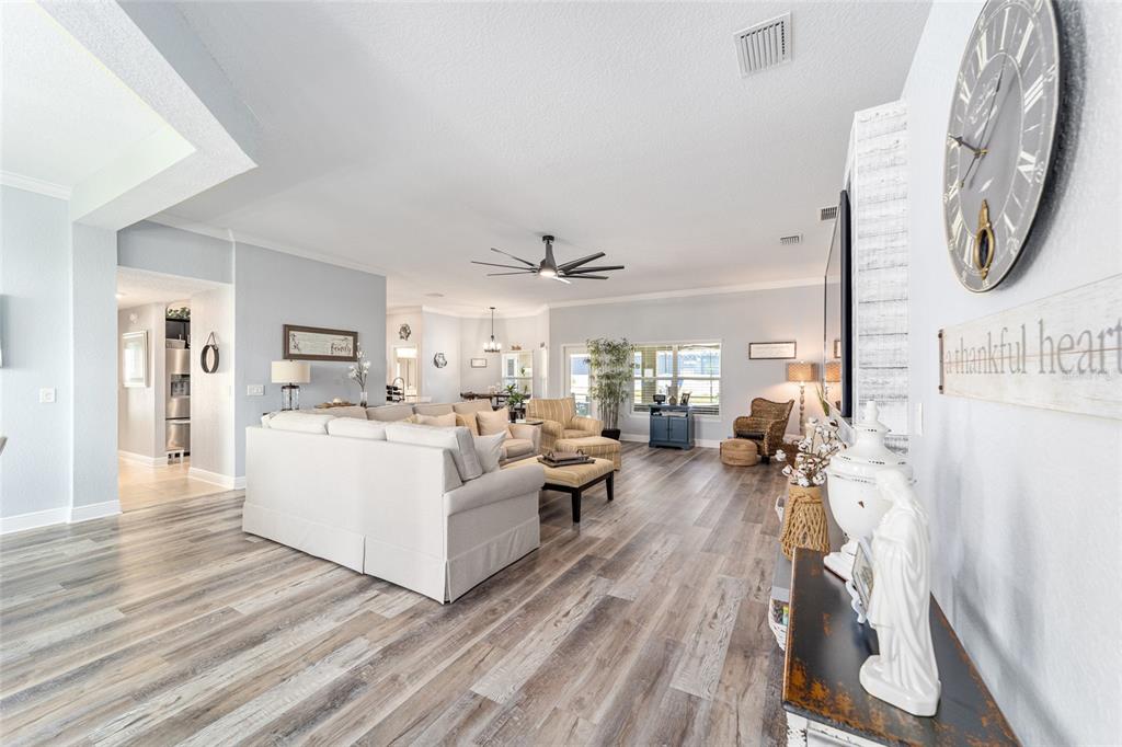 A spacious living room features light wood-look flooring, a large sectional sofa, and a ceiling fan — 6943 SE 11TH PLACE, OCALA, FL