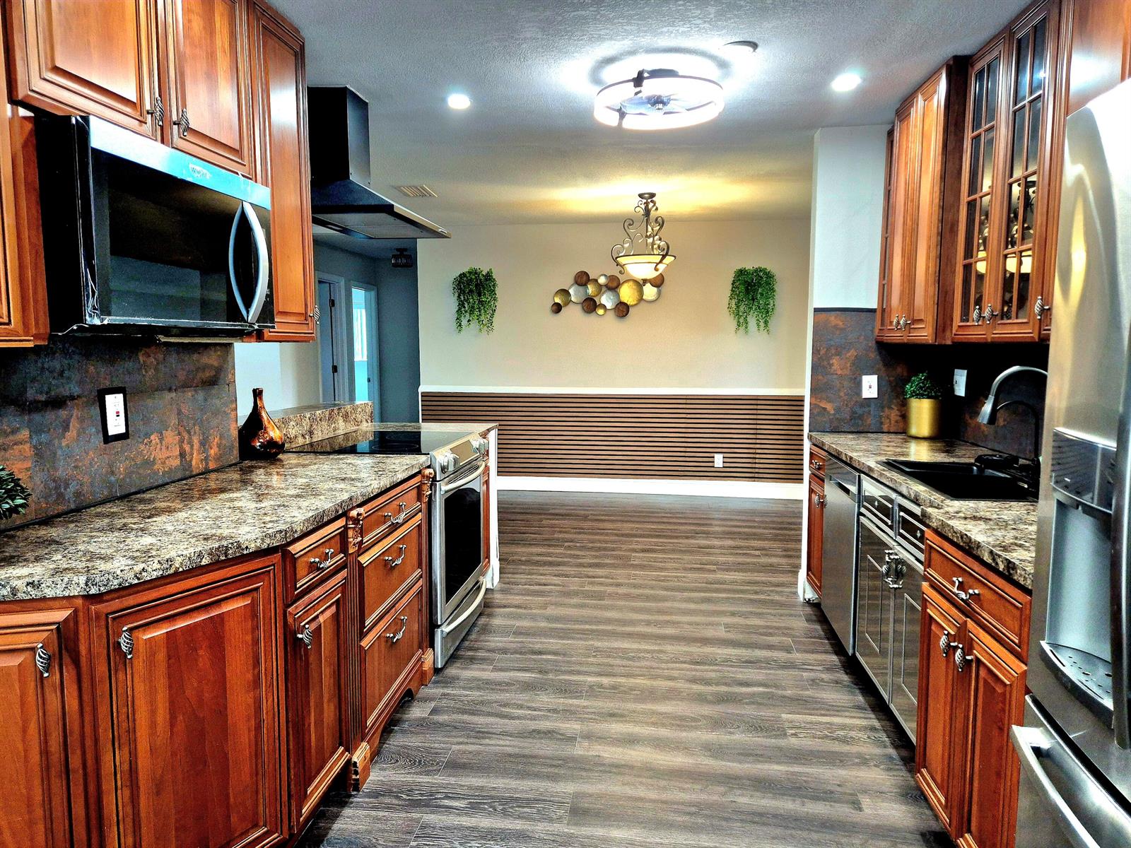 A galley kitchen features wood cabinets, granite countertops, stainless steel appliances, and wood-look flooring — 1015 NW 68th Avenue, Margate FL 33063, MARGATE, FL