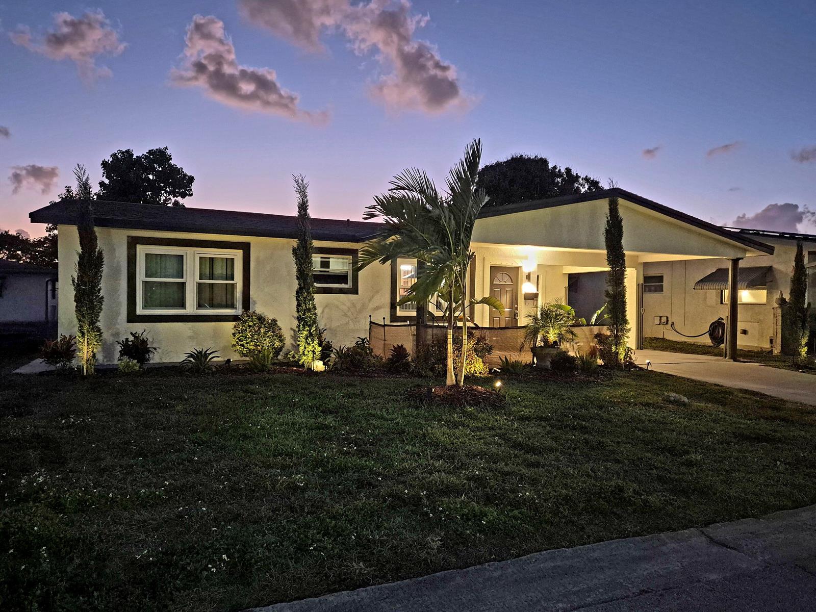 A single-story house with a carport and landscape lighting at dusk — 1015 NW 68th Avenue, Margate FL 33063, MARGATE, FL
