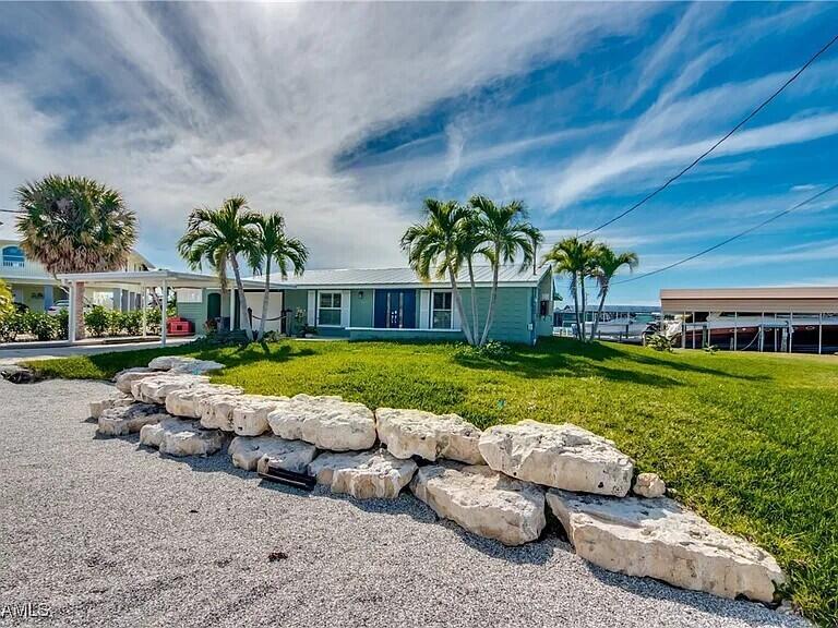 A light green house with a rock retaining wall and palm trees sits on a lawn — 2891 Cussell Drive, FL 33956, FL
