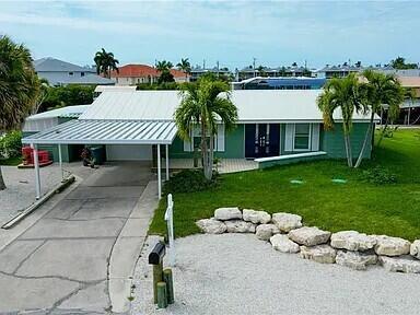 A single-story house with a white metal roof, carport, and palm trees in the front yard — 2891 Cussell Drive, FL 33956, FL