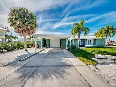 A single-story house with a carport, palm trees, and a concrete driveway under a blue sky — 2891 Cussell Drive, FL 33956, FL