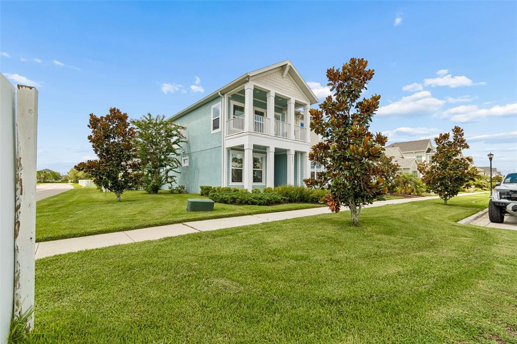 A light blue two-story house with a front porch and balcony sits on a lawn — 28692 COZY CREEK DRIVE, WESLEY CHAPEL, FL