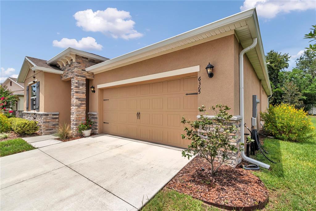 A tan stucco house exterior features a two-car garage, stone accents, and a concrete driveway — 6365 SW 88TH LOOP, OCALA, FL
