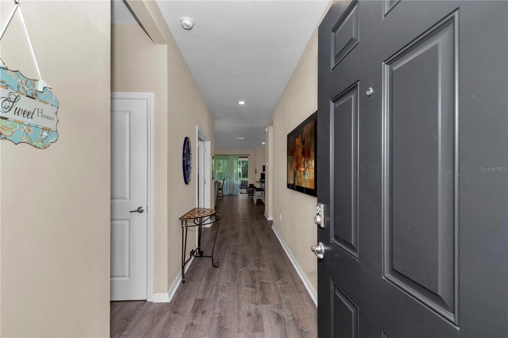 An entryway with wood-look flooring leads into a hallway with a dark door and artwork — 6365 SW 88TH LOOP, OCALA, FL