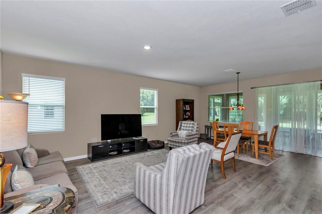 A living room with gray wood-look flooring, a television, and an adjacent dining area — 6365 SW 88TH LOOP, OCALA, FL