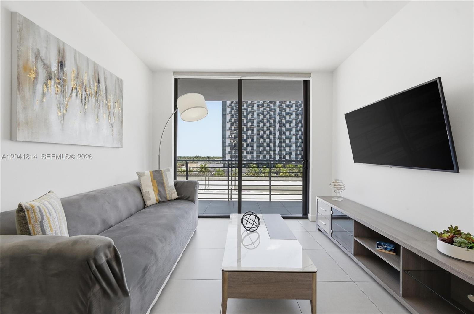 A modern living room features a gray sofa, coffee table, media console, and balcony access — 5350 NW 84th Ave # 504, Doral FL 33166, DORAL, FL
