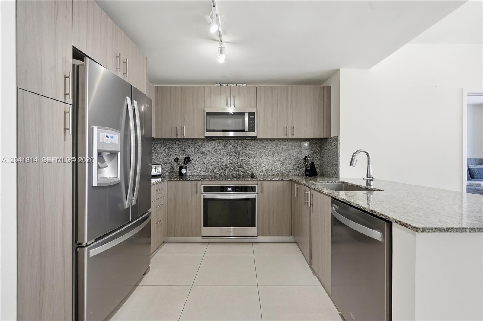 A modern kitchen features stainless steel appliances, light wood cabinets, and granite countertops — 5350 NW 84th Ave # 504, Doral FL 33166, DORAL, FL