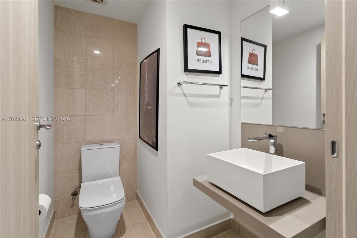 A modern bathroom features a white vessel sink, a toilet, and framed wall art — 1000 Brickell Plz # 3303, Miami FL 33131, MIAMI, FL