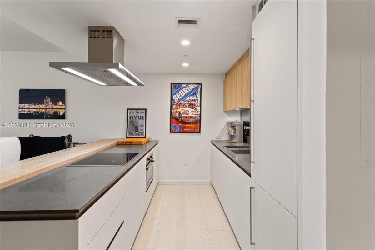 A modern galley kitchen features white cabinetry, dark countertops, and framed wall art — 1000 Brickell Plz # 3303, Miami FL 33131, MIAMI, FL