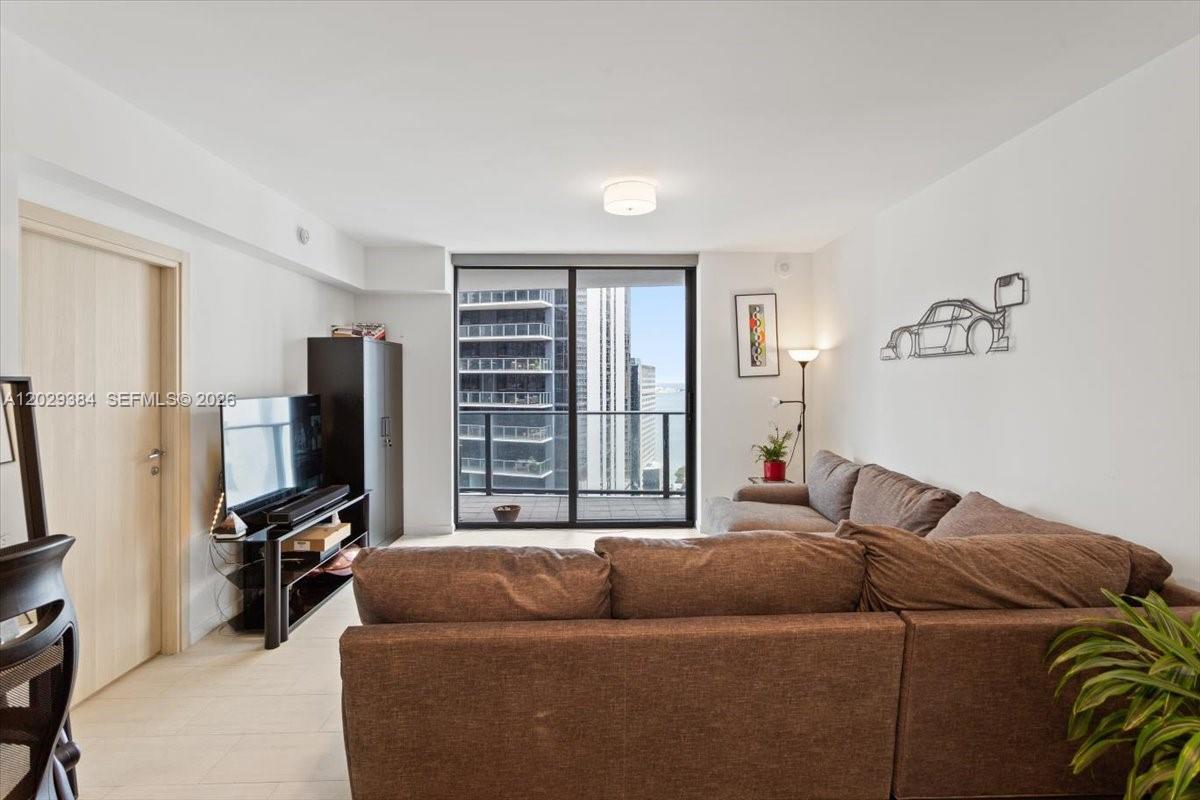 A living room features a brown sectional sofa, a television, and a balcony with city views — 1000 Brickell Plz # 3303, Miami FL 33131, MIAMI, FL