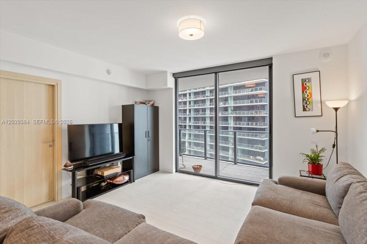 A living room features a grey sofa, a television on a stand, and a balcony — 1000 Brickell Plz # 3303, Miami FL 33131, MIAMI, FL