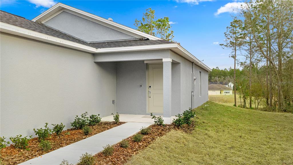 A gray stucco house exterior features a covered entryway with a light-colored front door — 8140 SW 44TH TERRACE, OCALA, FL