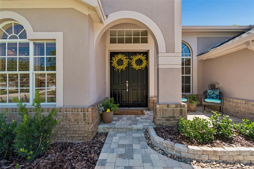 A paved walkway leads to a front entrance with double black doors and brick accents — 10423 GREENHEDGES DRIVE, TAMPA, FL