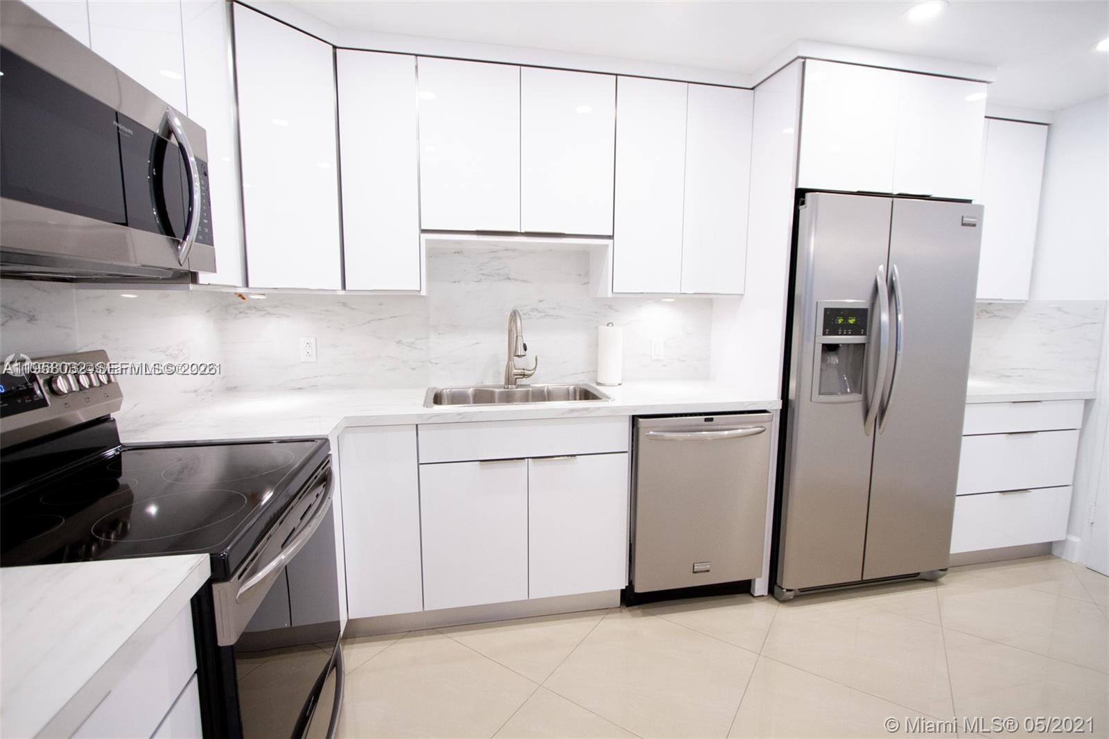 A modern kitchen features white cabinets, stainless steel appliances, and marble-patterned countertops and backsplash — 3801 S Ocean Dr, Hollywood FL 33019, HOLLYWOOD, FL