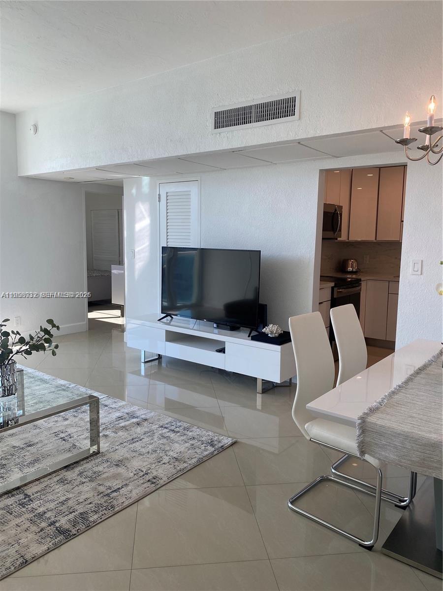 A living room features white tile floors, a white media console, and an adjacent kitchen — 3801 S Ocean Dr, Hollywood FL 33019, HOLLYWOOD, FL