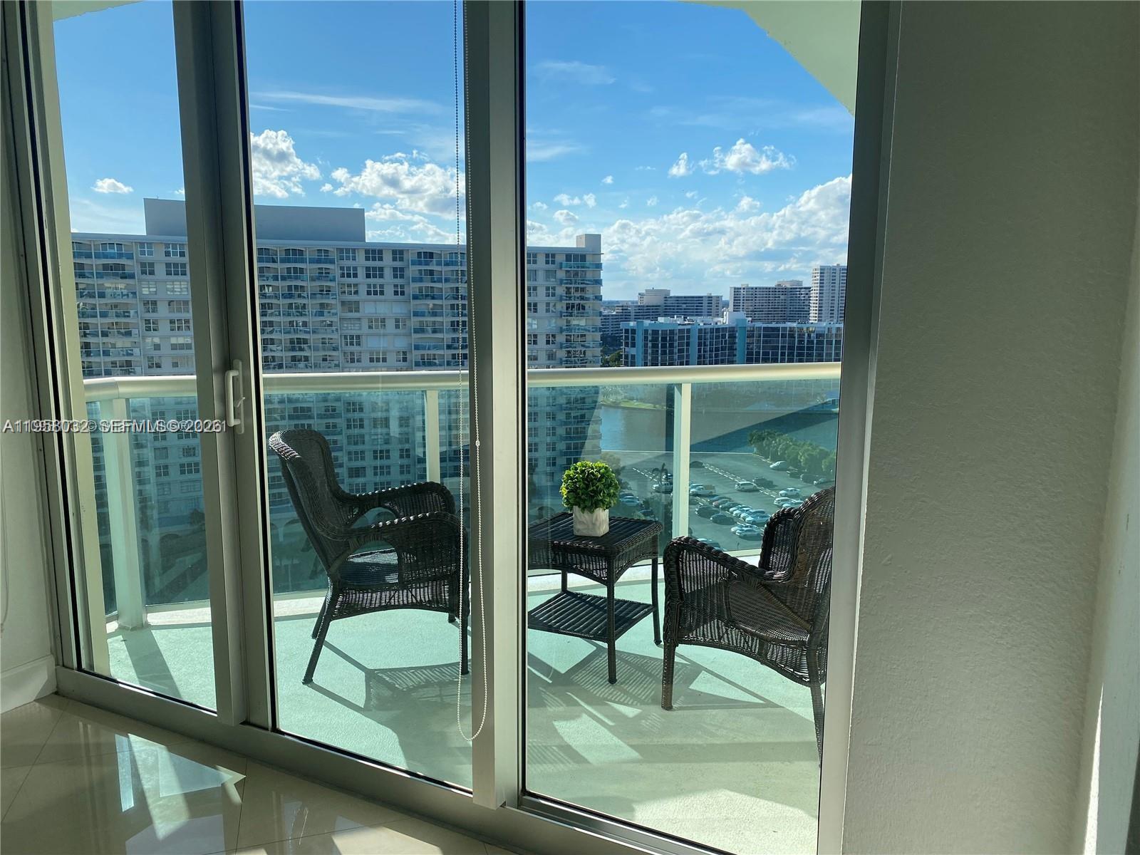 A balcony with two wicker chairs and a small table overlooks a city waterfront view — 3801 S Ocean Dr, Hollywood FL 33019, HOLLYWOOD, FL