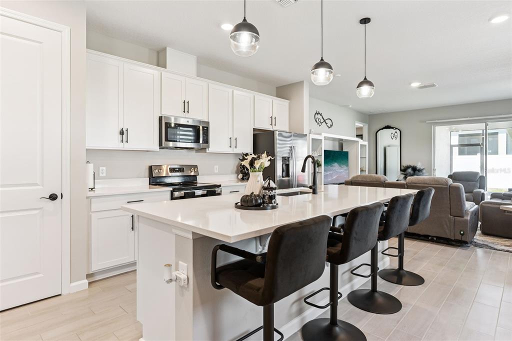 A modern kitchen features white cabinetry, a quartz island with bar stools, and stainless appliances — 891 BLUE CREEK DRIVE, HAINES CITY, FL