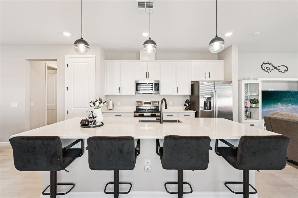 A modern kitchen features a large white island, dark bar stools, and white cabinetry — 891 BLUE CREEK DRIVE, HAINES CITY, FL