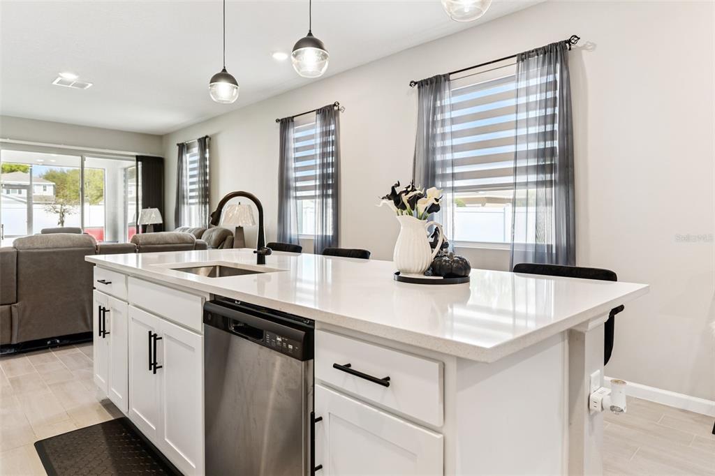 A kitchen island with a white countertop, sink, and dishwasher sits before a living area — 891 BLUE CREEK DRIVE, HAINES CITY, FL