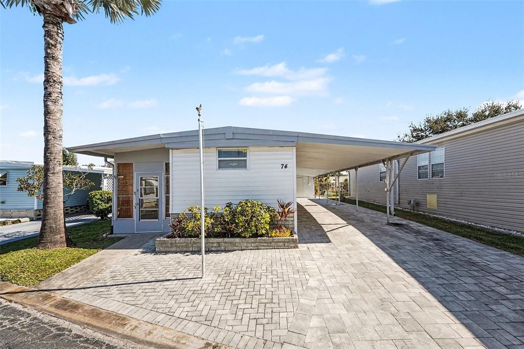 A single-story mobile home features a paved driveway, a carport, and a small front garden — 9790 66TH STREET N UNIT 74, PINELLAS PARK, FL