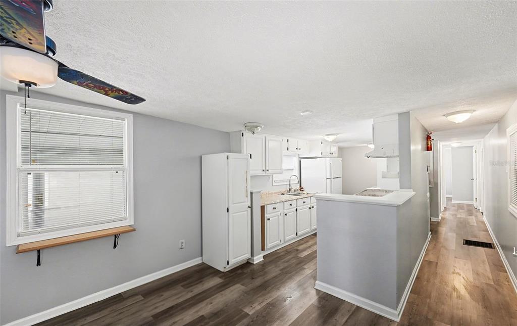A kitchen with white cabinets, light countertops, and wood-look flooring opens to a hallway — 9790 66TH STREET N UNIT 74, PINELLAS PARK, FL