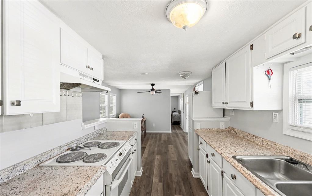 A kitchen with white cabinets, granite countertops, and stainless steel appliances leads into a living area — 9790 66TH STREET N UNIT 74, PINELLAS PARK, FL