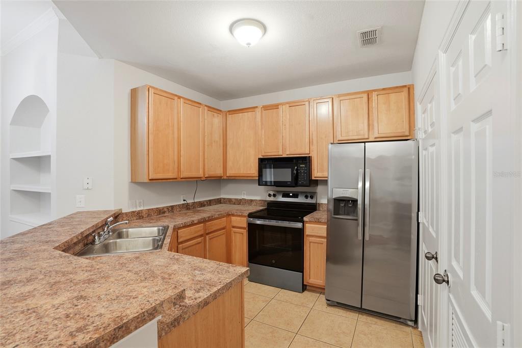 A kitchen features light wood cabinets, laminate countertops, stainless steel appliances, and tile flooring — 9916 COURTNEY PALMS BOULEVARD UNIT 302, TAMPA, FL