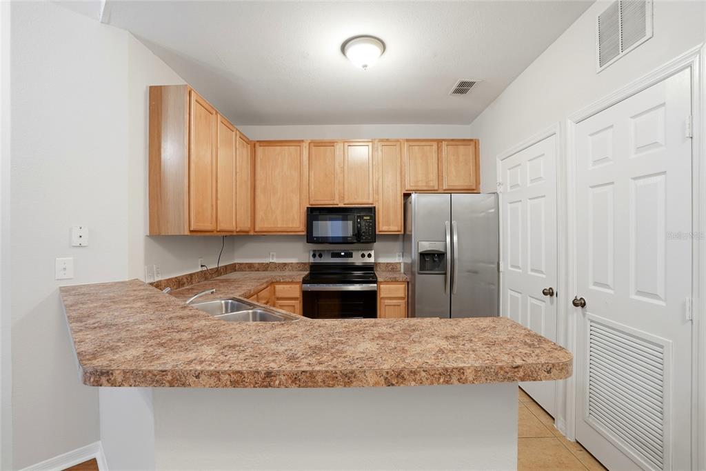 A kitchen features light wood cabinets, laminate countertops, and stainless steel appliances — 9916 COURTNEY PALMS BOULEVARD UNIT 302, TAMPA, FL