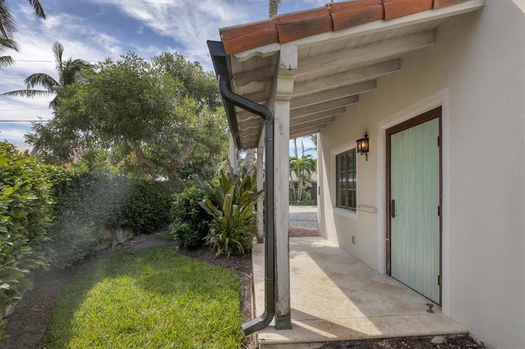 A covered patio with light-colored stone flooring leads to a light green door — 1021 10TH STREET W, BOCA GRANDE, FL