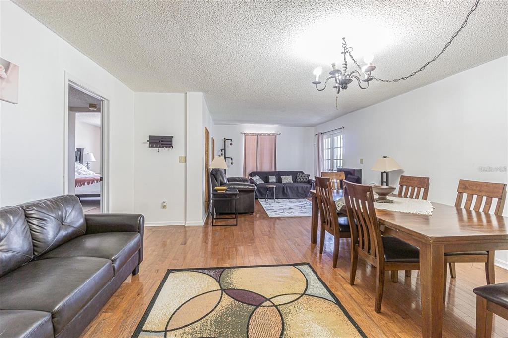 A living and dining area with hardwood floors, a chandelier, and two leather sofas — 14820 RUE DE BAYONNE UNIT 301, CLEARWATER, FL