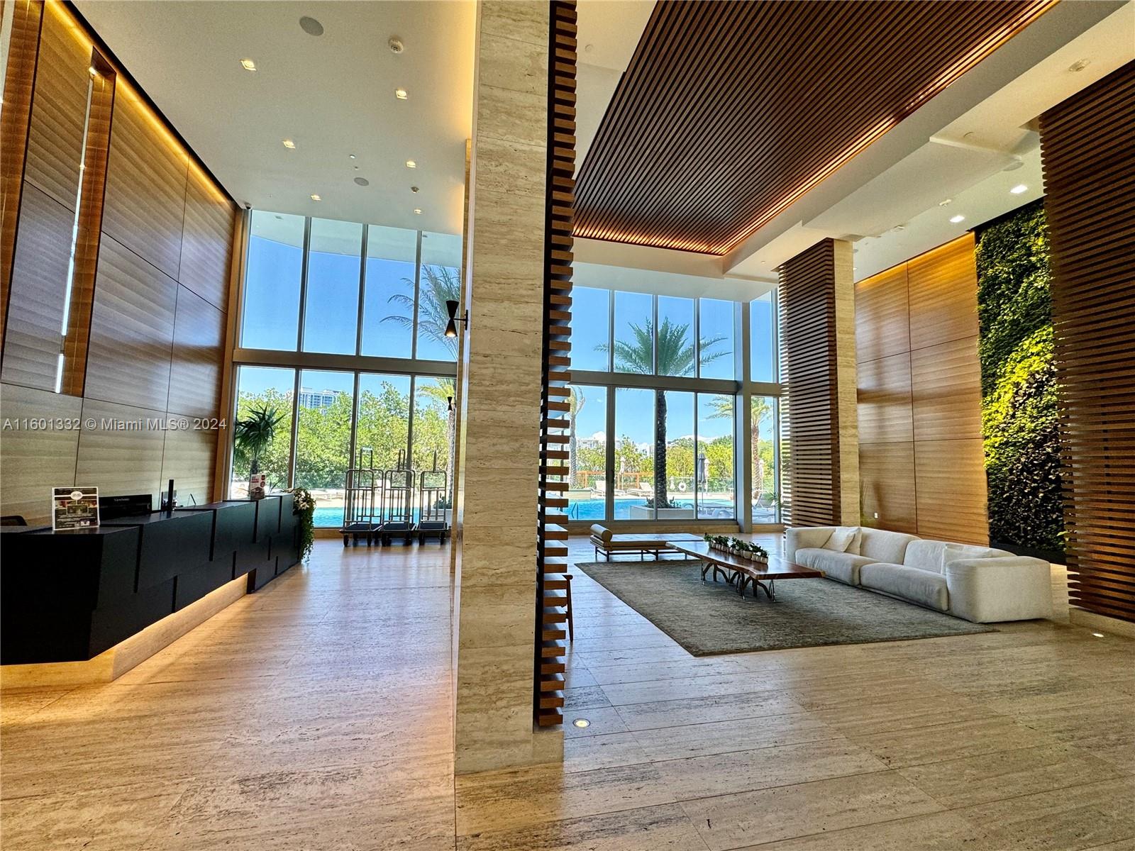 A modern building lobby features wood paneling, floor-to-ceiling windows, a living wall, and seating — 16385 Biscayne Blvd # 2421, North Miami Beach FL 33160, NORTH MIAMI BEACH, FL