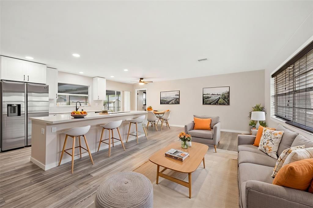 An open-concept living room and kitchen featuring light wood floors, white cabinetry, and neutral furniture — 1901 BRIARWOOD STREET, DUNEDIN, FL