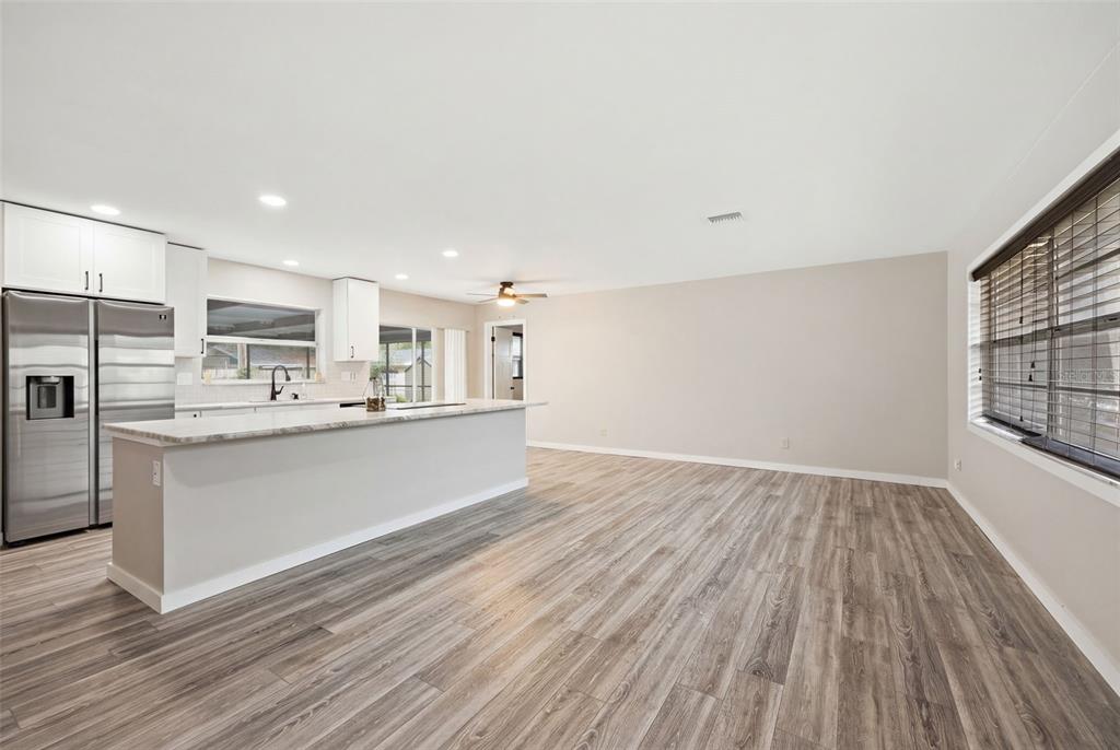 A kitchen with white cabinets and a large island opens into a spacious living area — 1901 BRIARWOOD STREET, DUNEDIN, FL