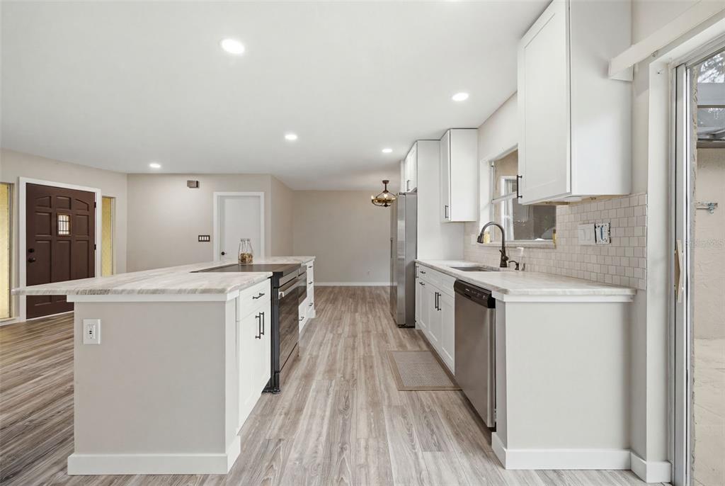 A kitchen features white cabinets, a stone-topped island with a range, and light wood flooring — 1901 BRIARWOOD STREET, DUNEDIN, FL