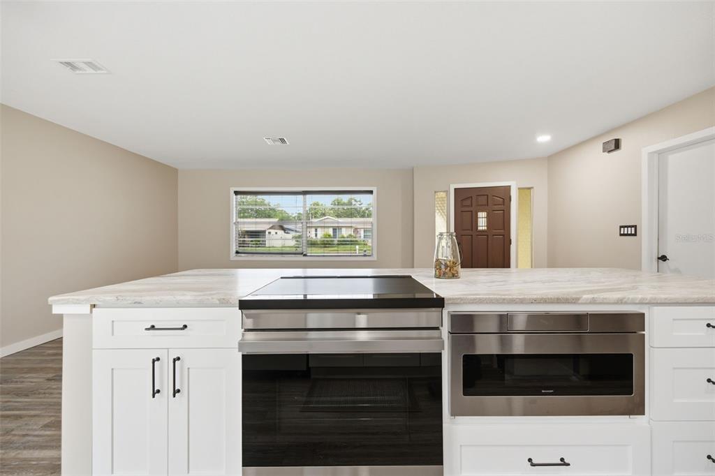 A kitchen island with a built-in oven and microwave features white cabinets and stone countertops — 1901 BRIARWOOD STREET, DUNEDIN, FL