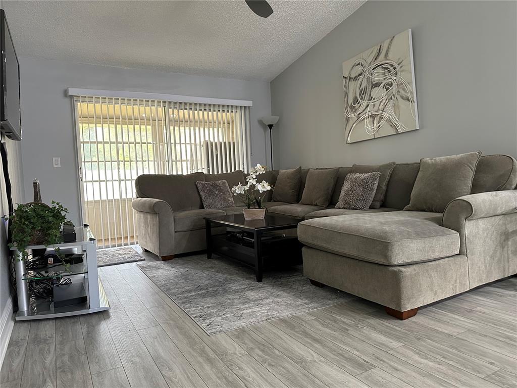 A living room features a gray sectional sofa, a coffee table, and wood-look flooring — 3198 CLAREMONT PLACE UNIT A, PALM HARBOR, FL