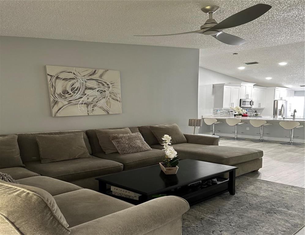 A living room features a large sectional sofa, a black coffee table, and an open kitchen — 3198 CLAREMONT PLACE UNIT A, PALM HARBOR, FL