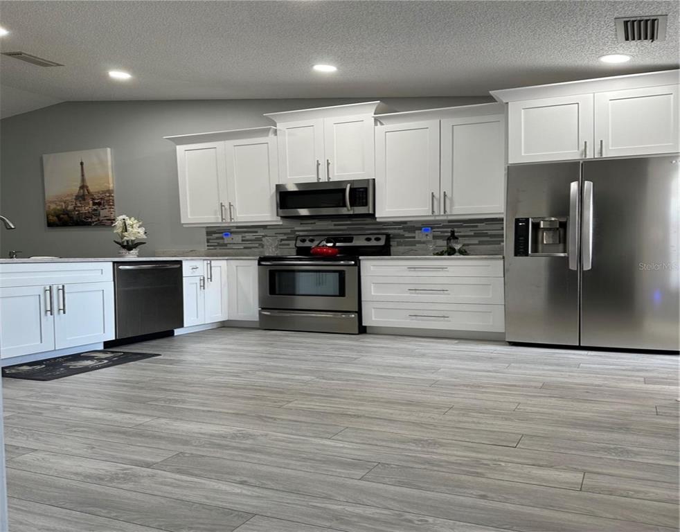 A modern kitchen features white cabinets, stainless steel appliances, and light-colored wood-look flooring — 3198 CLAREMONT PLACE UNIT A, PALM HARBOR, FL