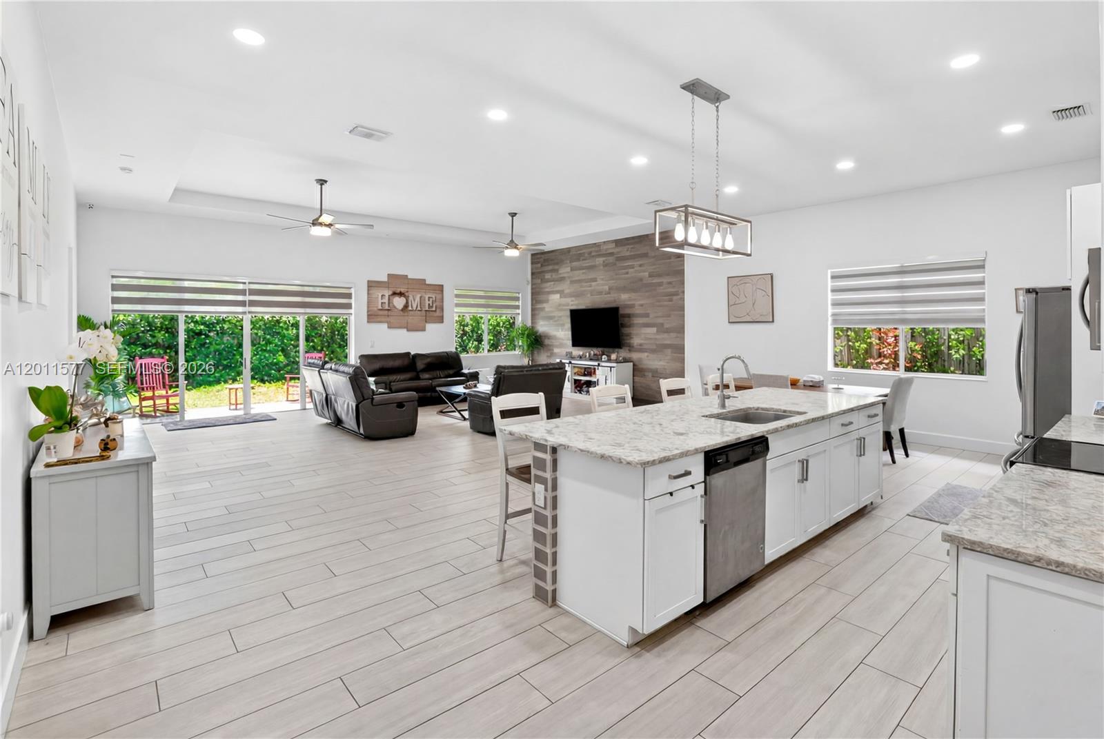 An open-concept living room and kitchen featuring light wood-look tile flooring and white cabinetry — 15012 SW 177th Ter, Miami FL 33187, MIAMI, FL