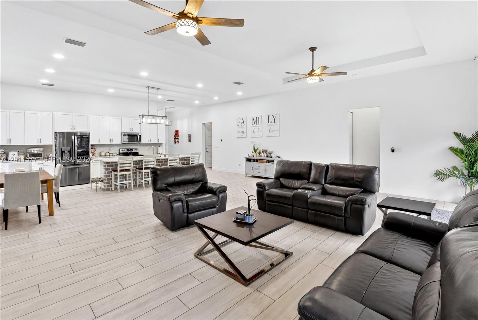 An open-concept living room and kitchen featuring white cabinetry, dark leather furniture, and tile flooring — 15012 SW 177th Ter, Miami FL 33187, MIAMI, FL
