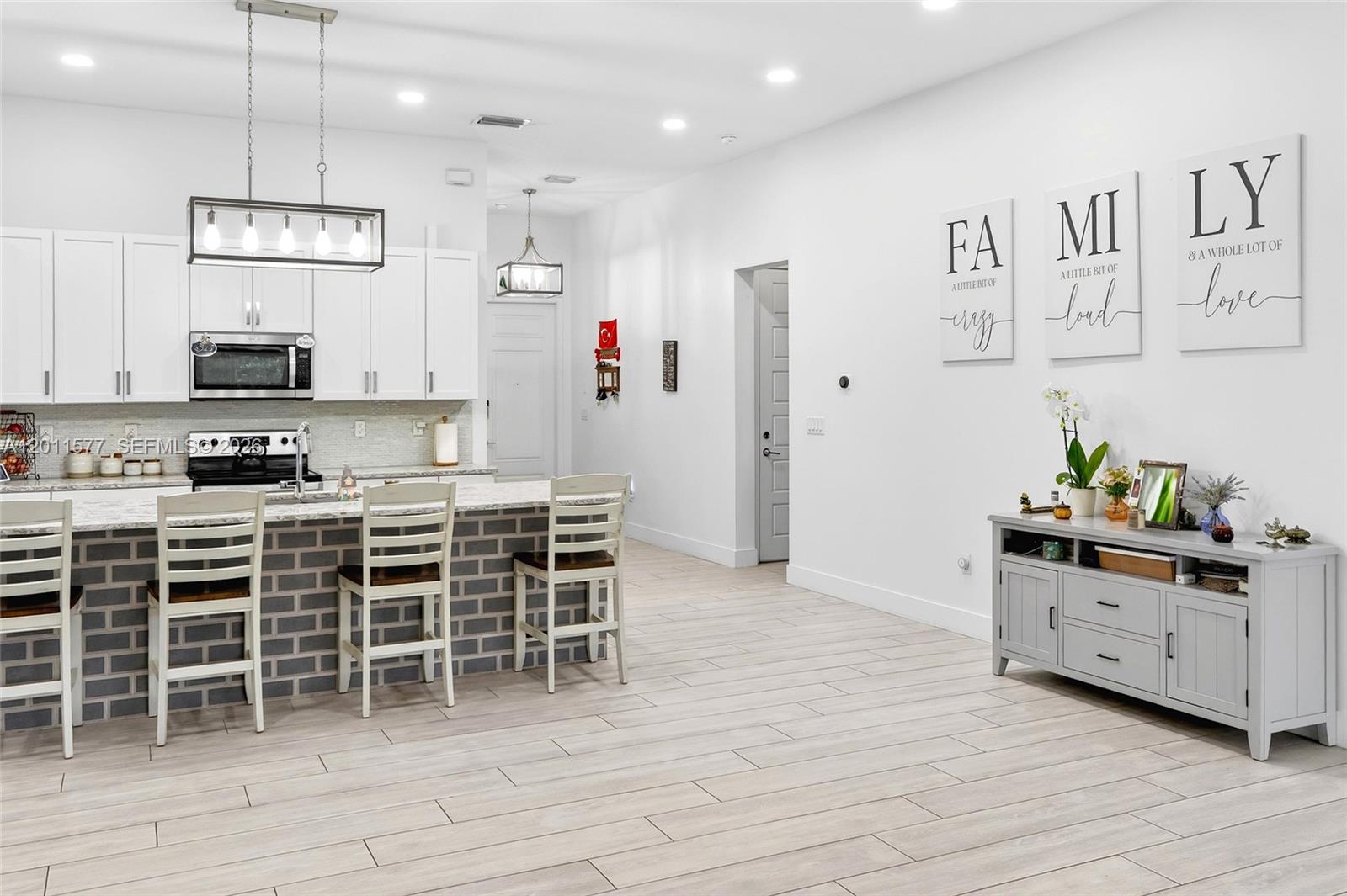 A modern kitchen features white cabinetry, a gray brick-faced island with bar stools, and wood-look flooring — 15012 SW 177th Ter, Miami FL 33187, MIAMI, FL
