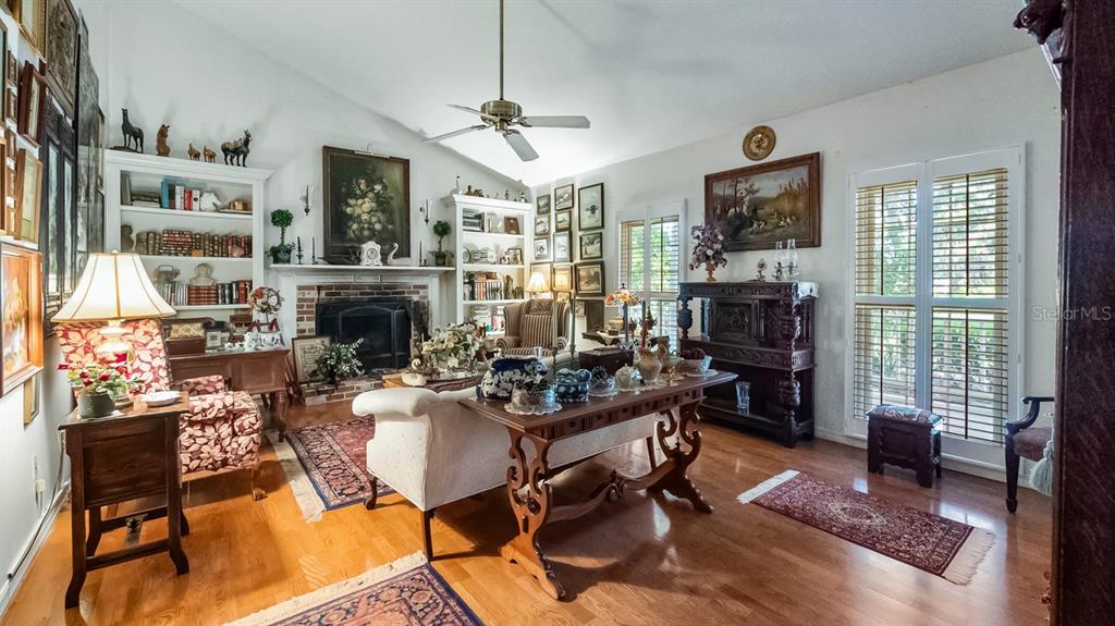 A living room features a brick fireplace, built-in bookshelves, hardwood floors, and a ceiling fan — 403 MISSION LANE, HOWEY IN THE HILLS, FL
