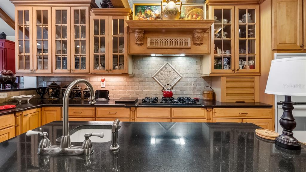 A kitchen features light wood cabinets, a black granite island, and a tiled backsplash — 403 MISSION LANE, HOWEY IN THE HILLS, FL