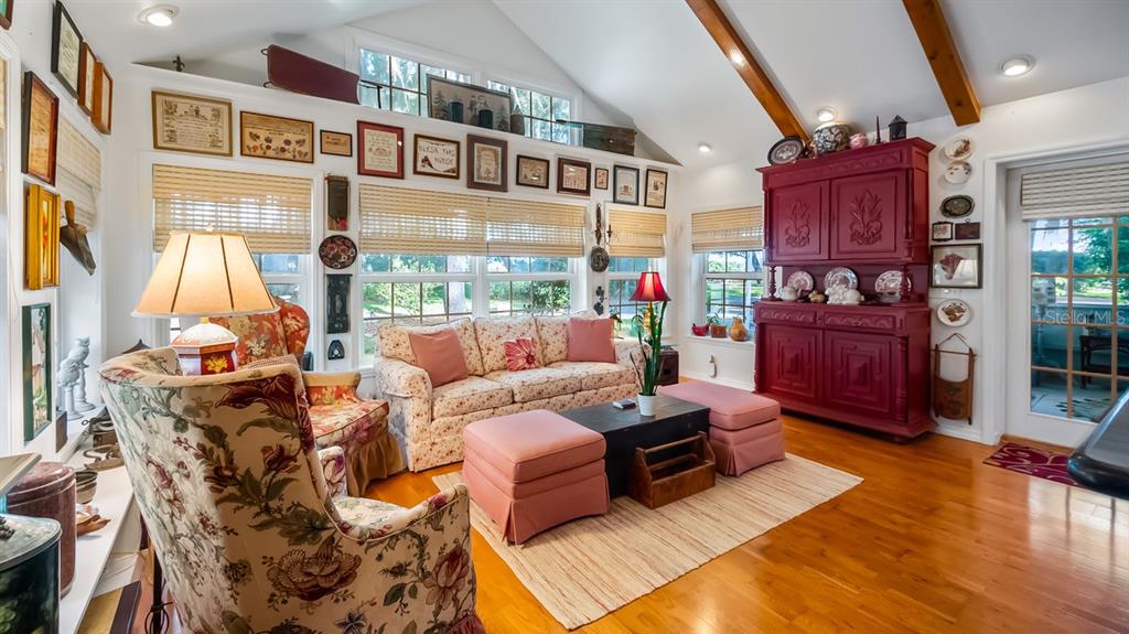 A sunroom features a vaulted ceiling with wood beams, floral furniture, and a red hutch — 403 MISSION LANE, HOWEY IN THE HILLS, FL